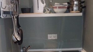 A compact kitchen with a sink, a stove, and a microwave. There are utensils hanging on the wall and a bowl on the countertop. - Gästehaus Sonne (Triefenstein)