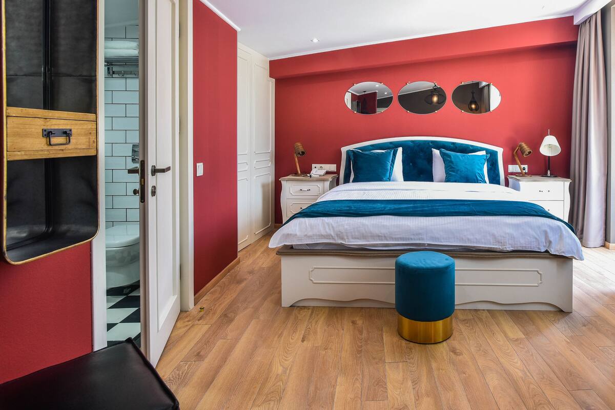 Ein Schlafzimmer mit einem Bett, Nachttischen, einem Spiegel und einem Hocker.