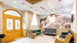 Eine großzügige Lobby mit Holztür, gepolsterten Sitzgelegenheiten, Wandgemälde und Fliesenboden.