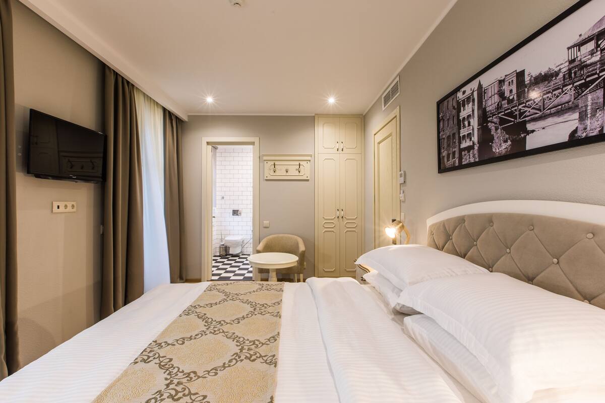 Ein Hotelzimmer mit einem Bett, einem Fernseher, einem Sessel, einem Kleiderschrank und einem gerahmten Bild an der Wand.