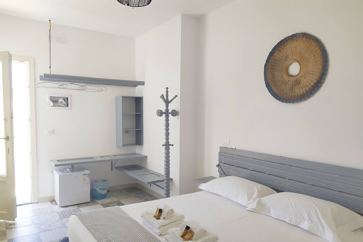 Une chambre d’hôtel comprenant un lit, un bureau, un miroir, un porte-manteau et un élément de décoration circulaire fixé au mur.