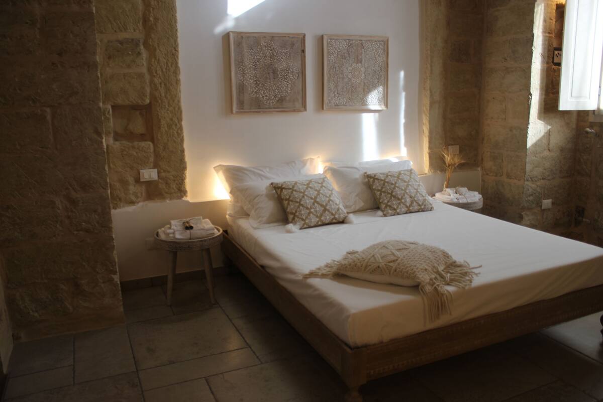 Une chambre avec un grand lit, deux tables de chevet et un mur en pierre.