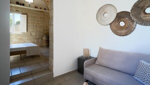 A room with a stone wall, a bed, a sofa, and decorative wall art. - Li Perrini Boutique B&B (Vernole)