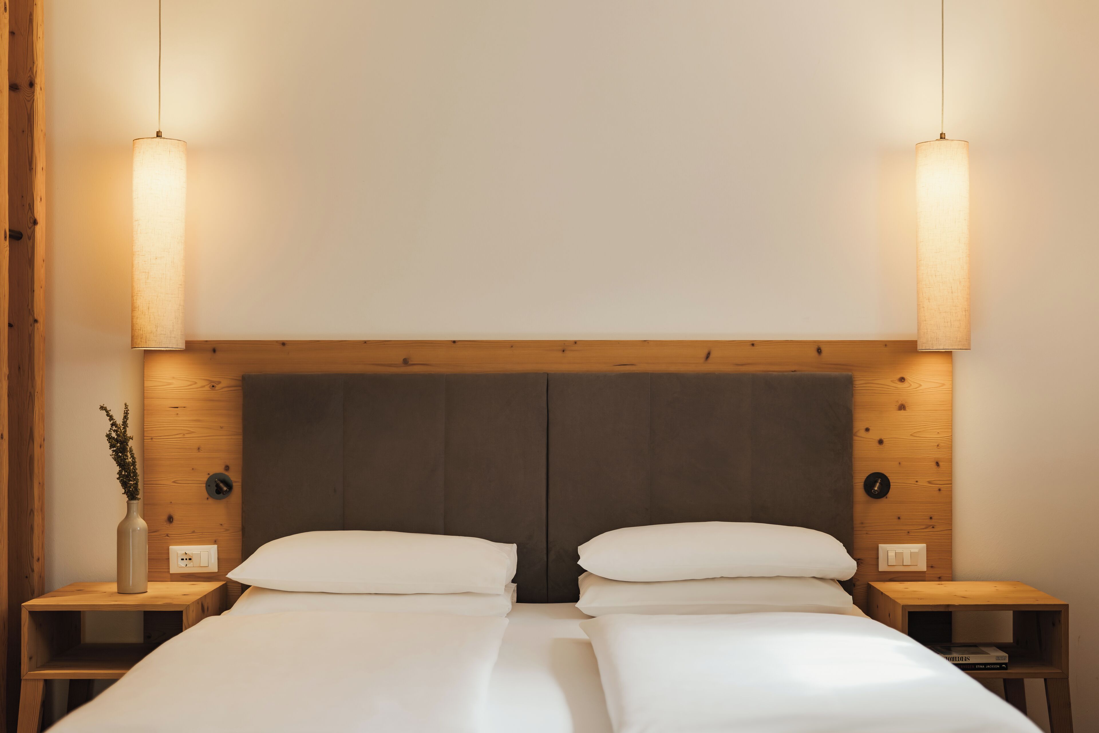 A double bed with a wooden headboard, two bedside tables, and wall-mounted lamps.