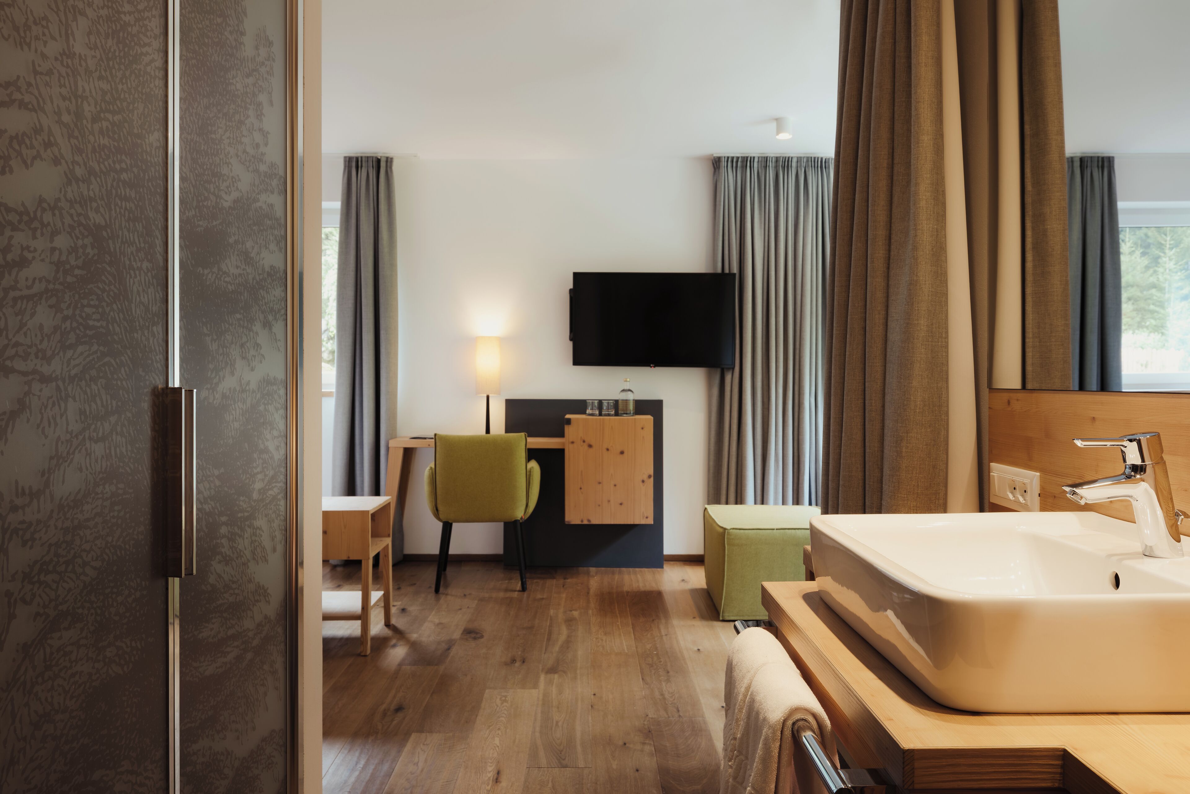 Un baño de hotel moderno con tocador de madera, un lavamanos grande y un televisor de pantalla plana montado sobre el espejo.
