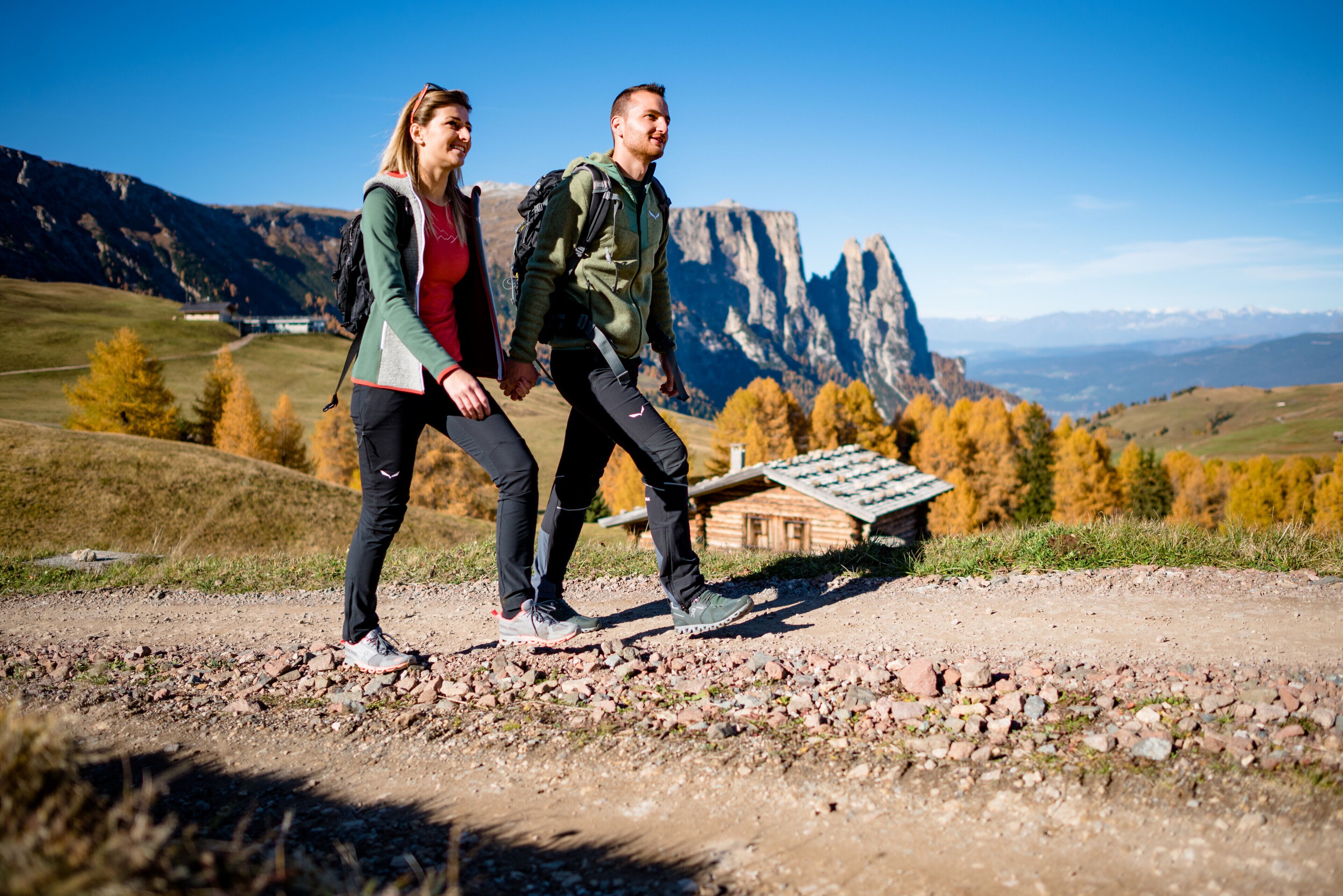 Two people hiking on a rocky trail with a mountainous landscape in the background.