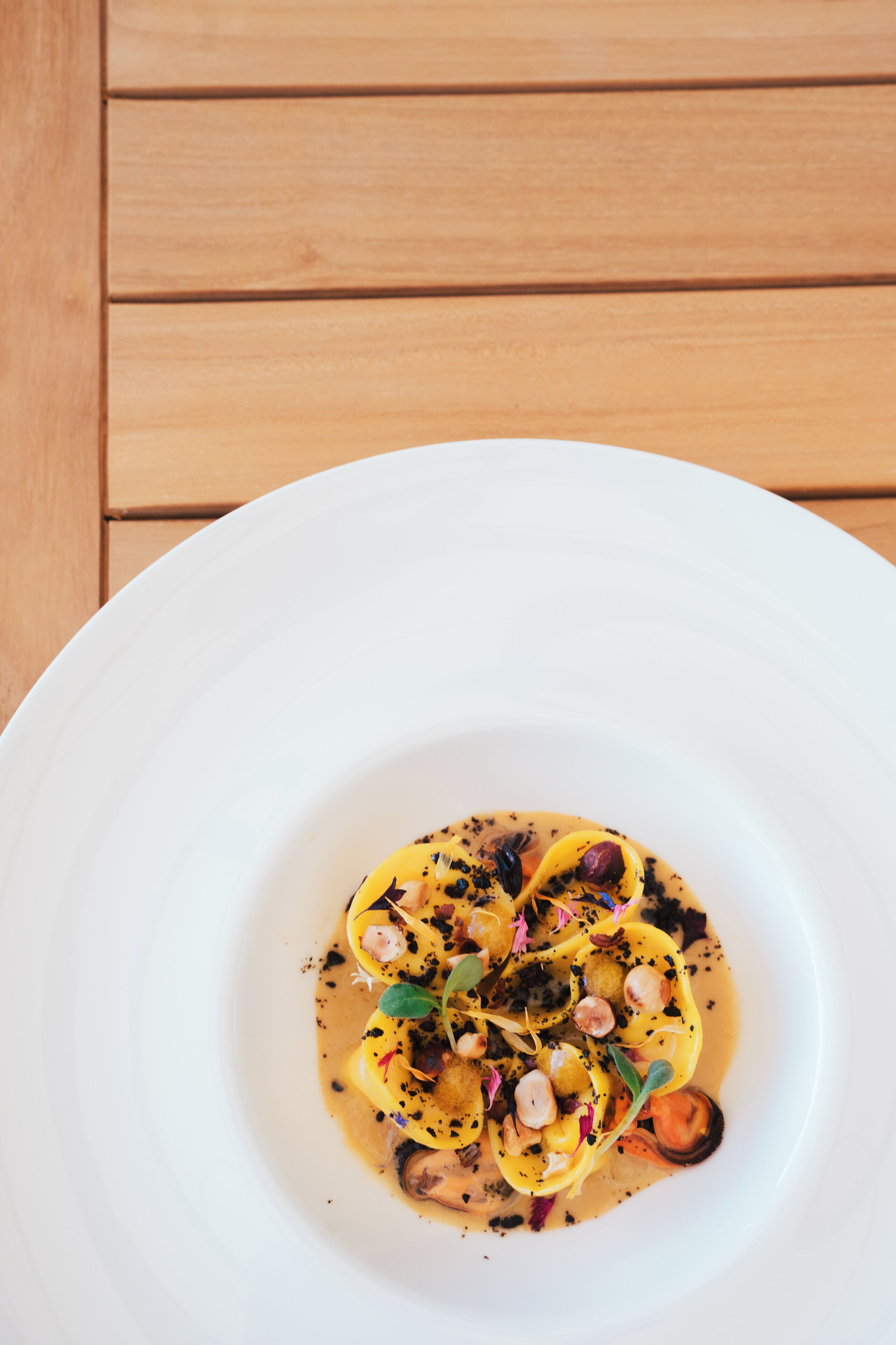 Une assiette blanche sur laquelle est présentée une spécialité culinaire, le tout posé sur une table en bois.