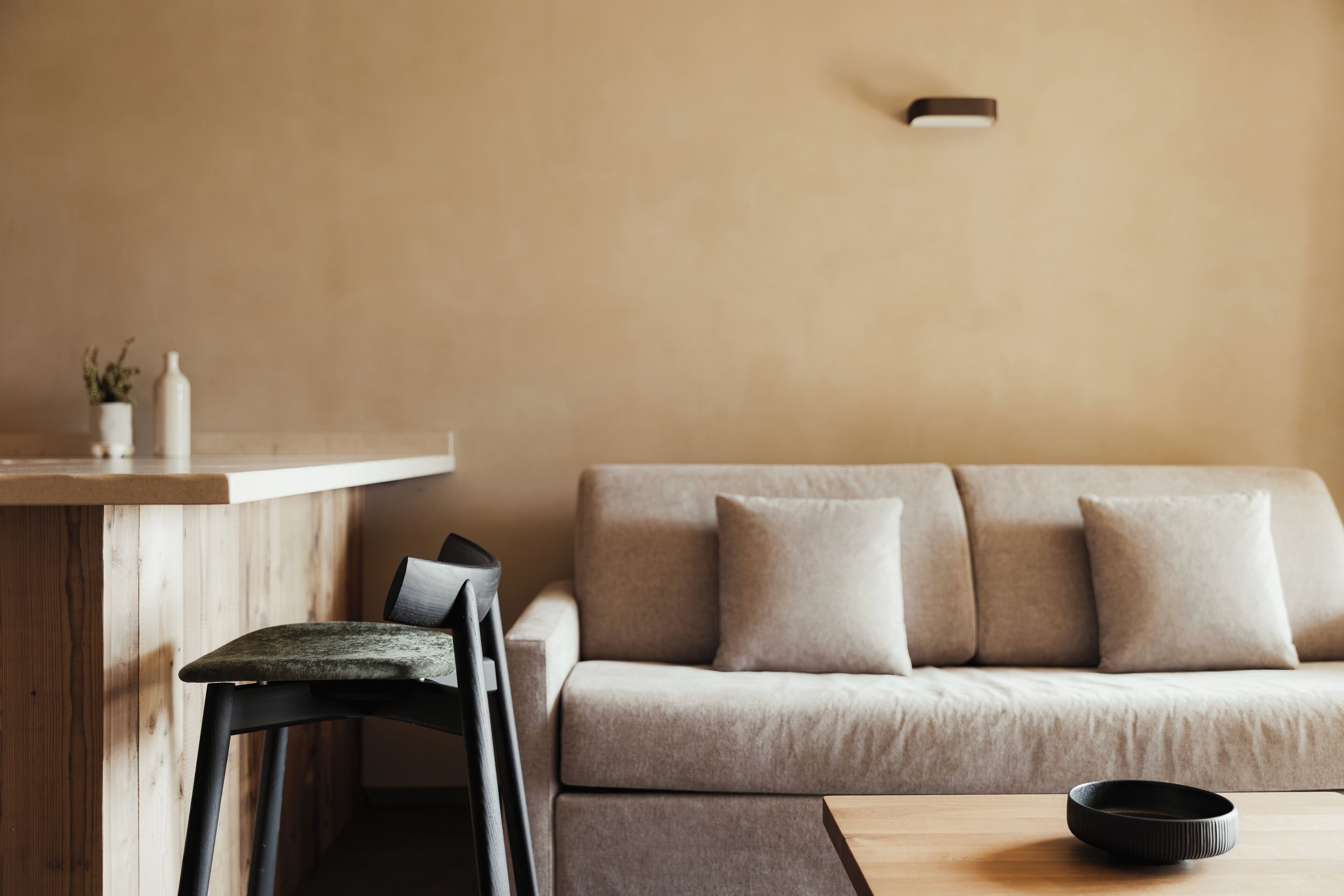 Un salon moderne avec une table en bois, une chaise noire et un canapé beige.