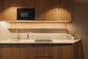 Una cocina moderna con armarios de madera, microondas integrado, pileta doble y una pequeña planta en maceta.