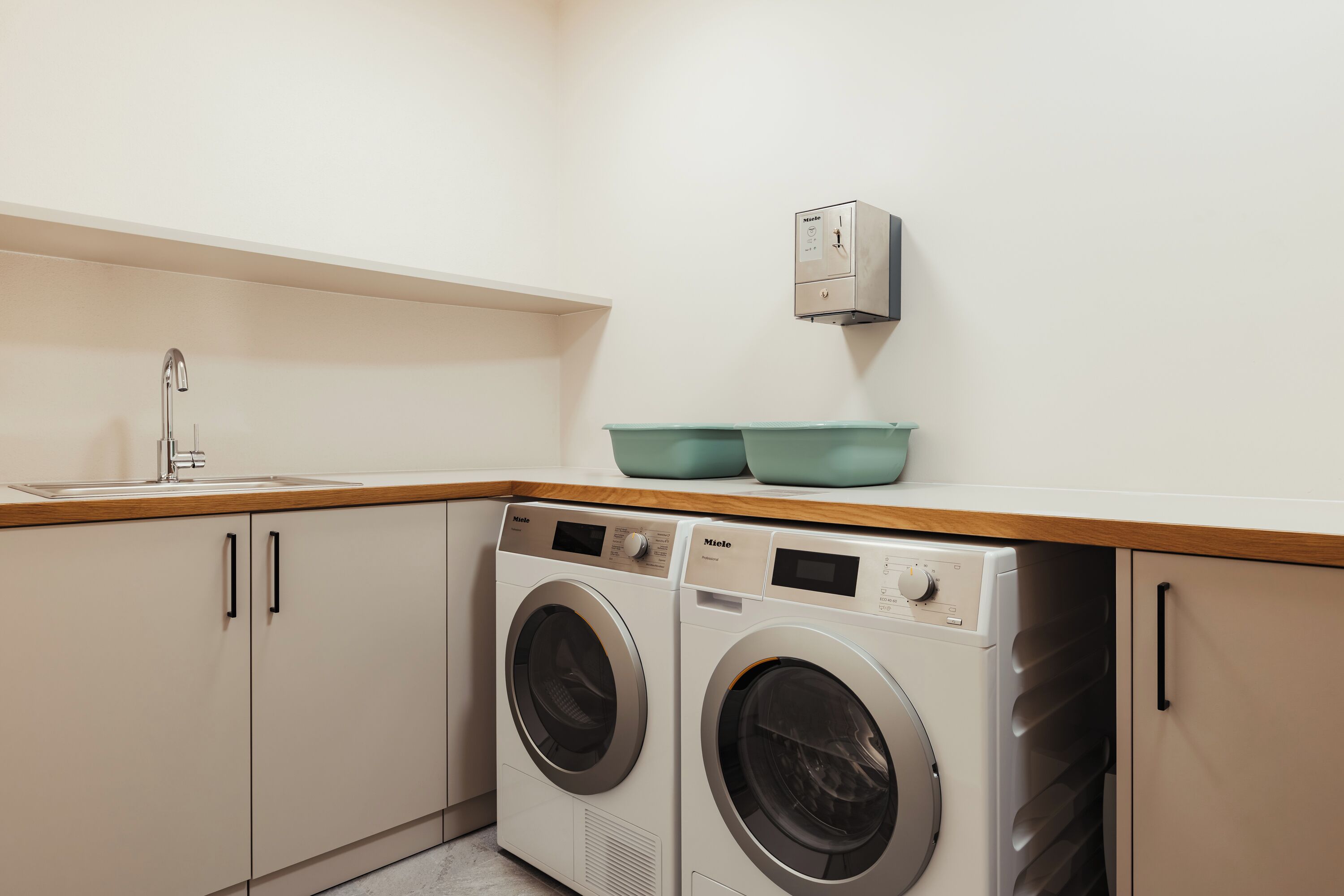 Une petite buanderie équipée de deux machines à laver à chargement frontal, d’un évier et d’un radiateur fixé au mur.