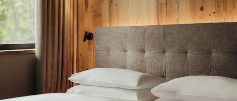 A neatly made bed with white linens and pillows, a grey upholstered headboard, and a wooden wall panel.