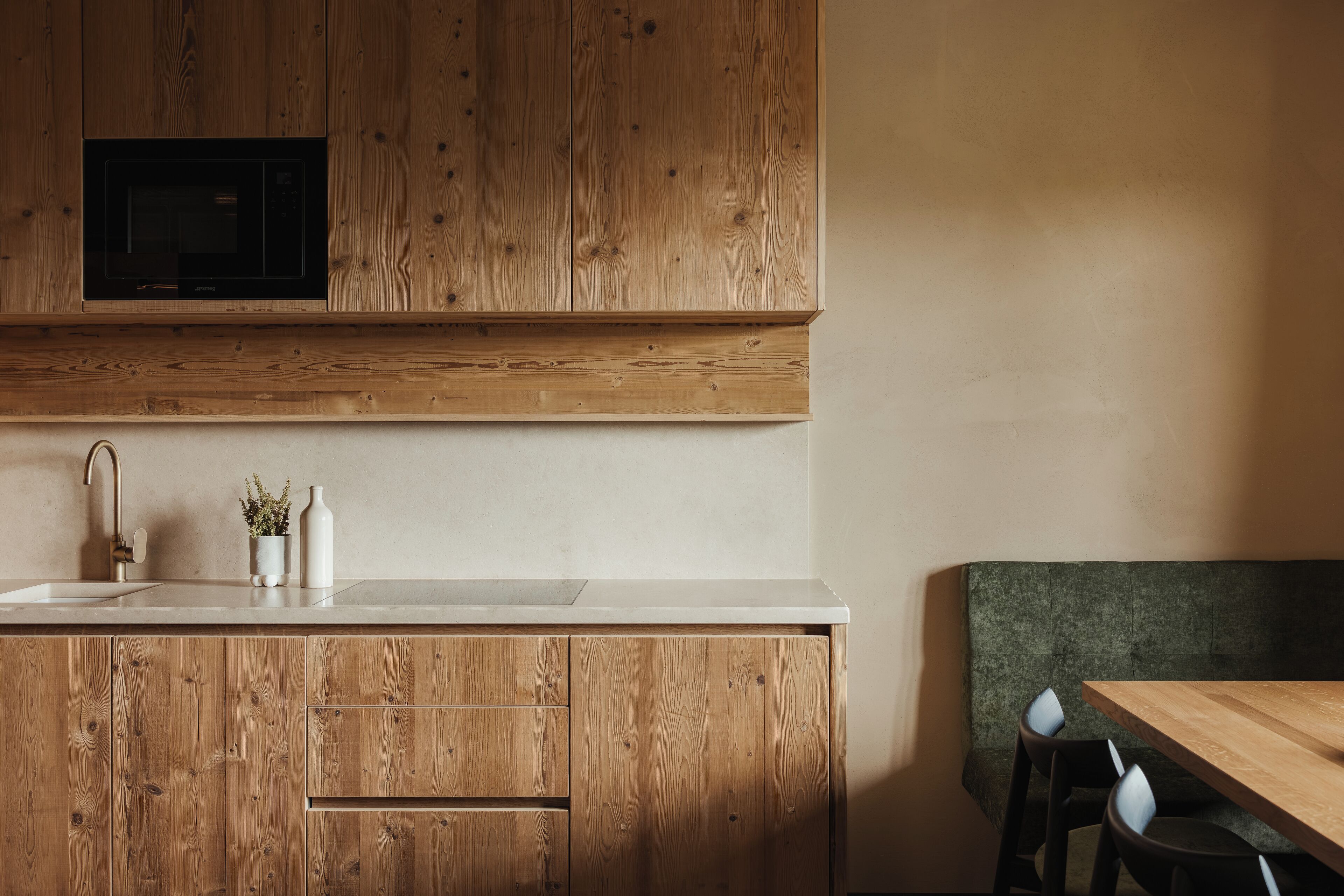 A kitchen with wooden cabinets, a microwave, a sink, and a green cushioned bench.