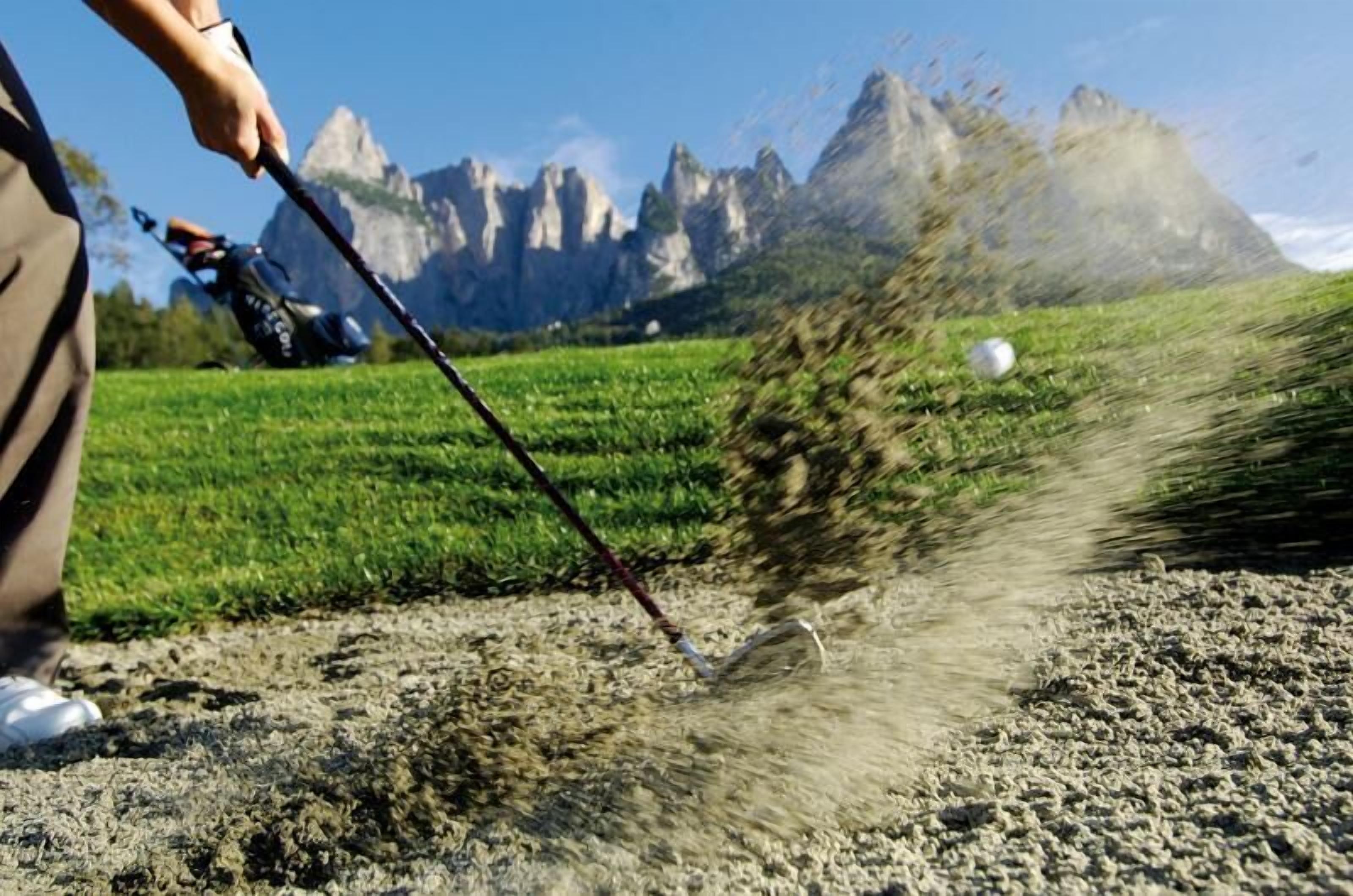 A person using a golf club on a golf course with a mountainous backdrop.
