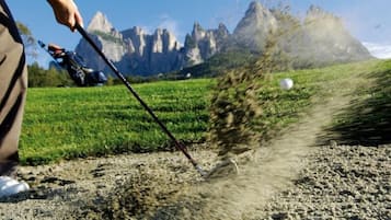 A person using a golf club on a golf course with a mountainous backdrop.