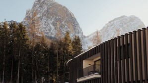 En moderne bygning med balkon, omgivet af sneklædte træer og bjerge.