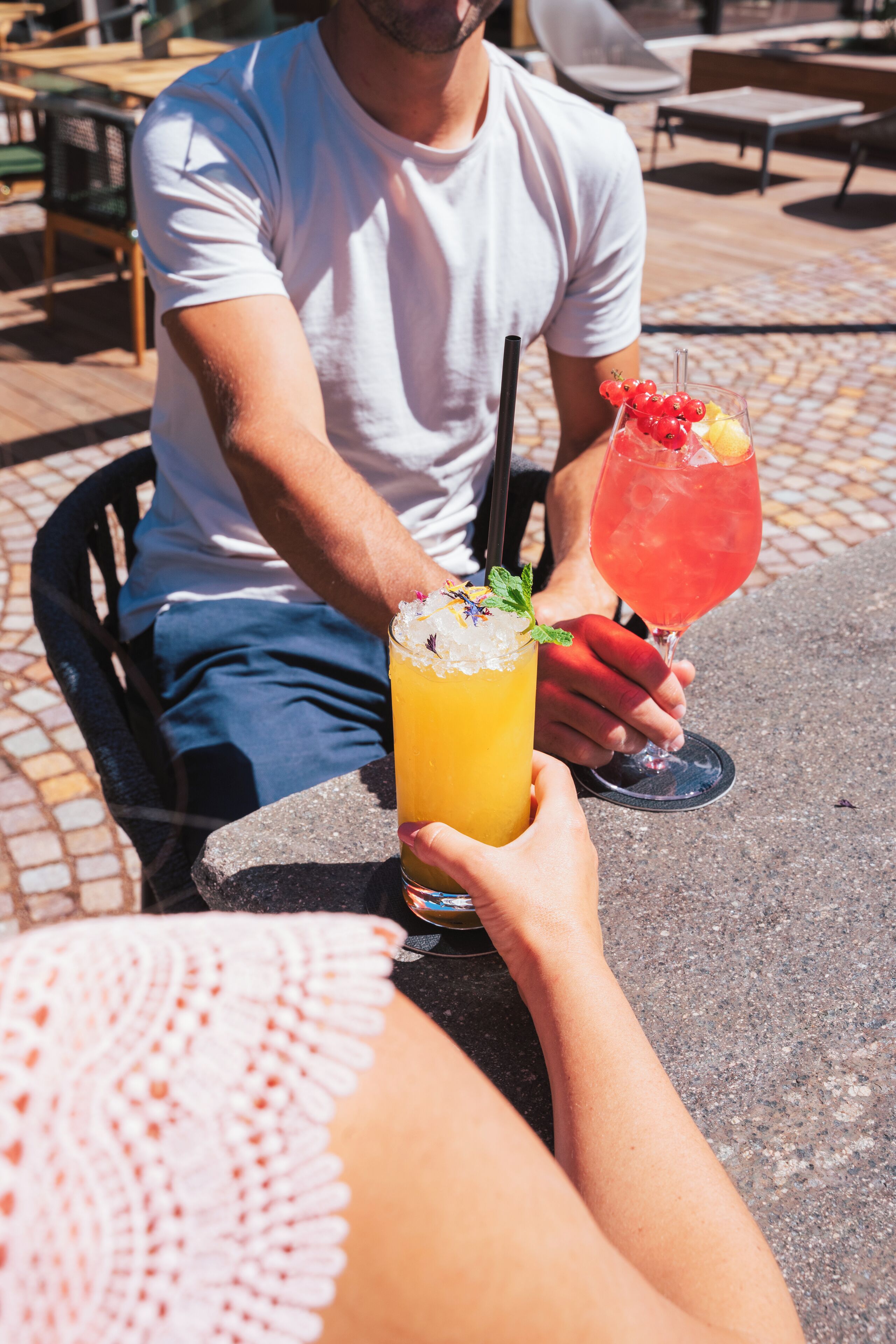 Una persona sentada en una mesa al aire libre, con dos bebidas: una en un vaso alto y otra en un vaso bajo, cada una con un popote.