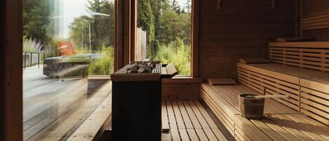 A wooden sauna with benches and a sauna table, large windows offering a view of trees and a deck outside.