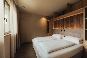 Un dormitorio con dos camas, cabecero de madera, estanterías empotradas y una ventana con cortinas.