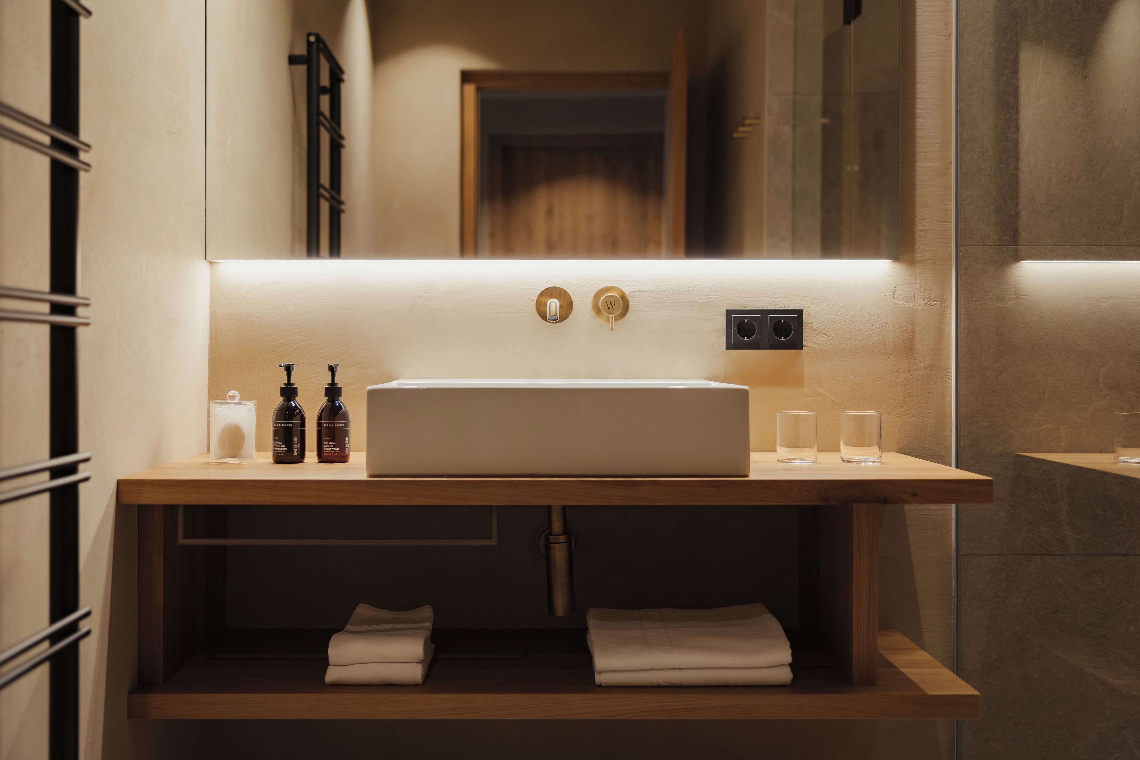 Un baño moderno con tocador de madera, un espejo grande y un lavamanos integrado.