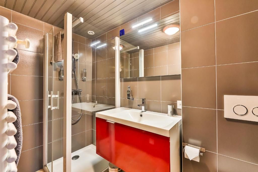 A modern bathroom with a glass shower enclosure, a white sink, and a red vanity.