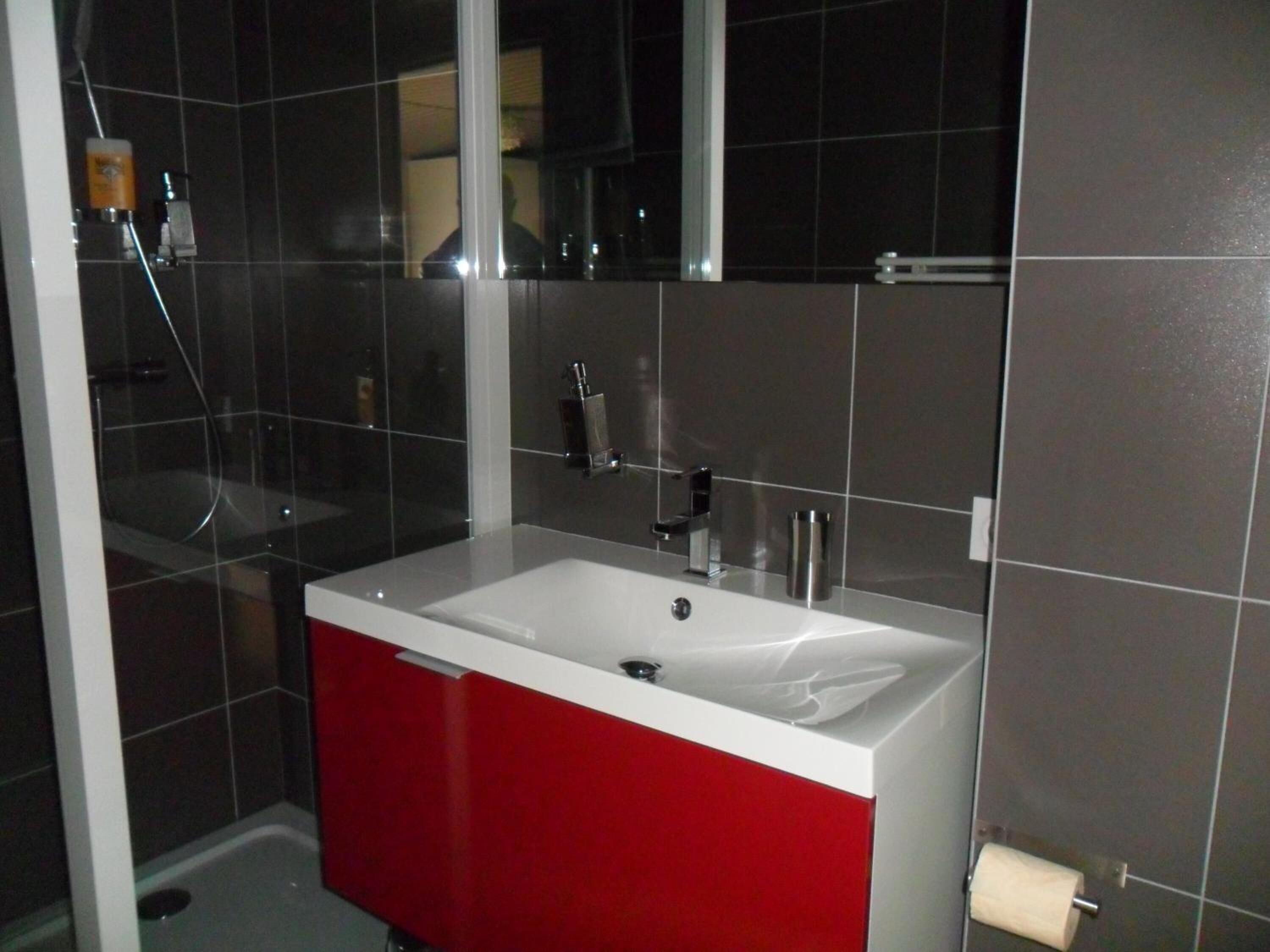 A bathroom with a white sink, red cabinet, and a mirror above the sink.