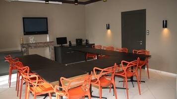 A conference room with a long table, orange chairs, a flat-screen TV, a fireplace, and a door.