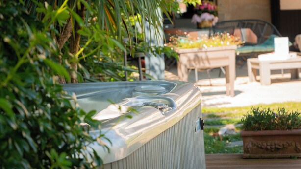 A hot tub in a garden setting with a patio area, outdoor furniture, and potted plants. - Studios Marie Barrault (Les Herbiers)