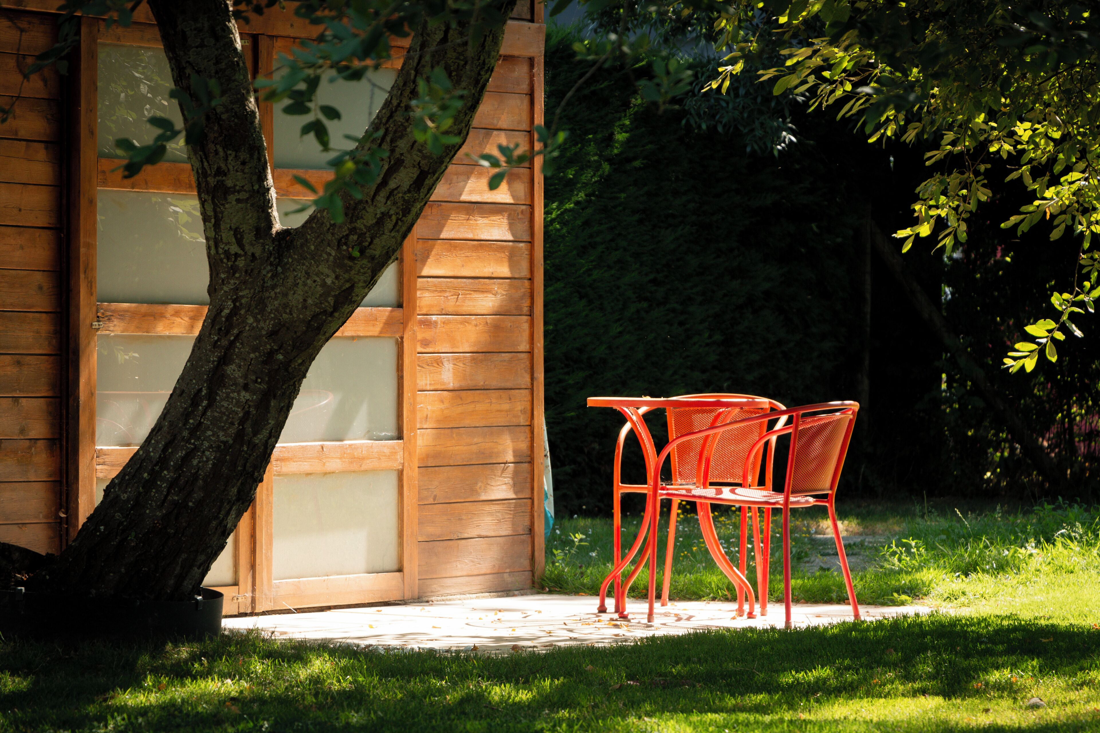 Ein Holzhaus mit Glastür und einer gepflasterten Terrasse mit zwei roten Stühlen.