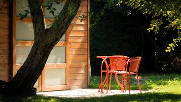 A wooden building with a glass door and a paved patio area with two red chairs.