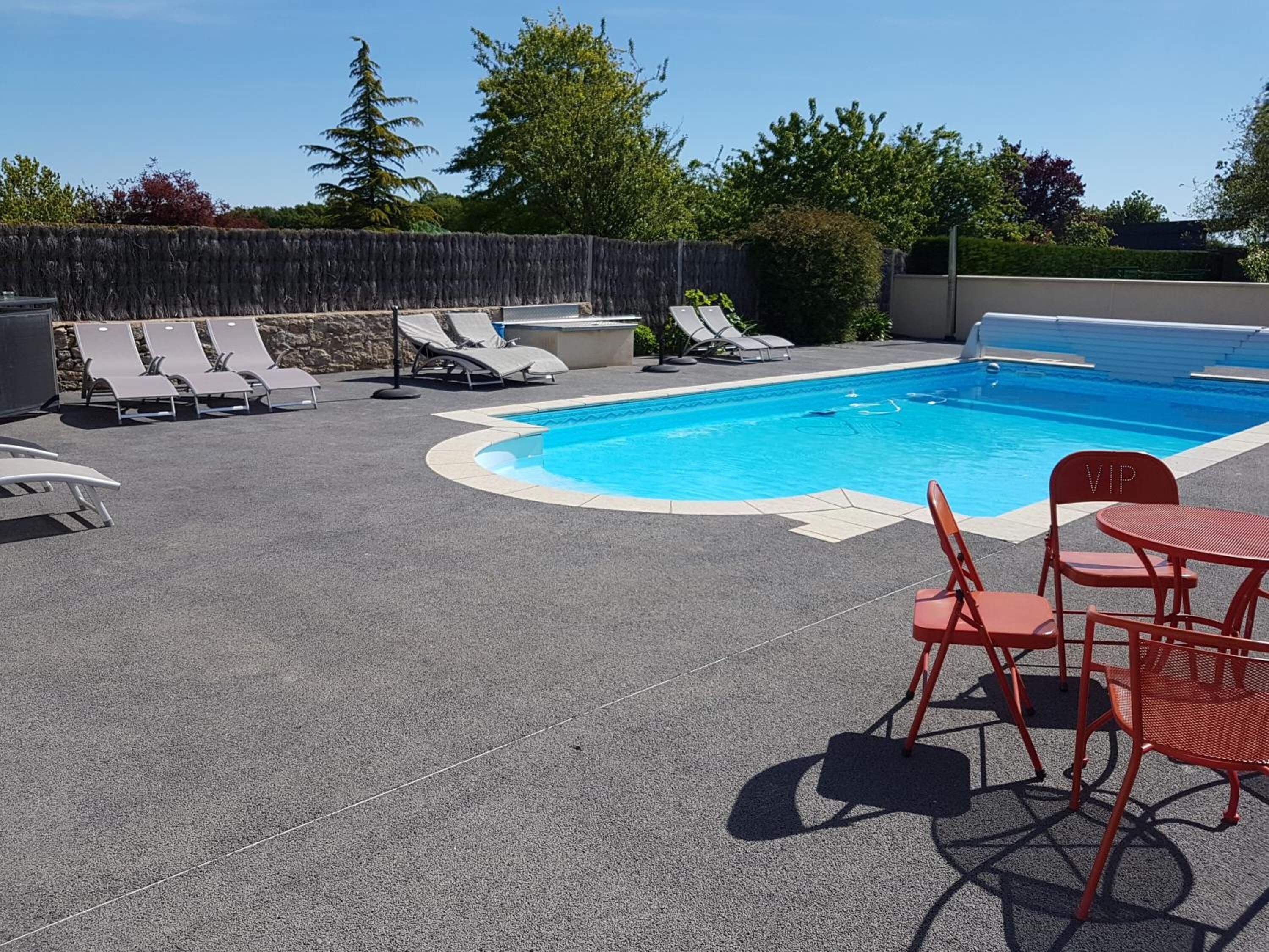 A swimming pool with lounge chairs and a table, surrounded by a stone wall and trees.