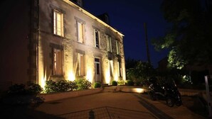 A historic building with illuminated windows and a paved driveway. - Studios Marie Barrault (Les Herbiers)