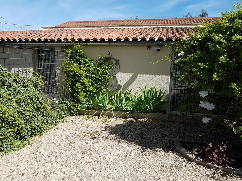 Una casa con techo de tejas, camino de entrada de grava y jardín con diversas plantas y flores.