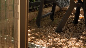 A metal table and chairs in a garden area with a view of a blue car and a building in the background. - Studios Marie Barrault (Les Herbiers)