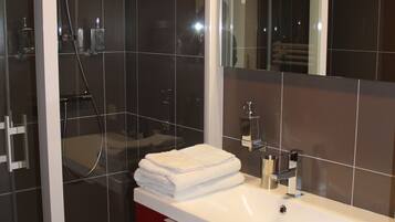 A modern bathroom with a glass-enclosed shower, a white sink with a red cabinet, and a large mirror.