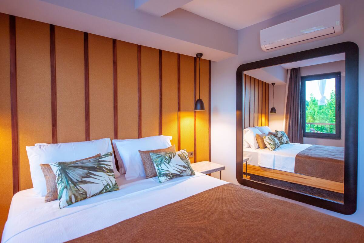 Habitación de hotel con una cama grande, una mesita de noche, una lámpara de pared y un espejo grande que refleja la habitación.