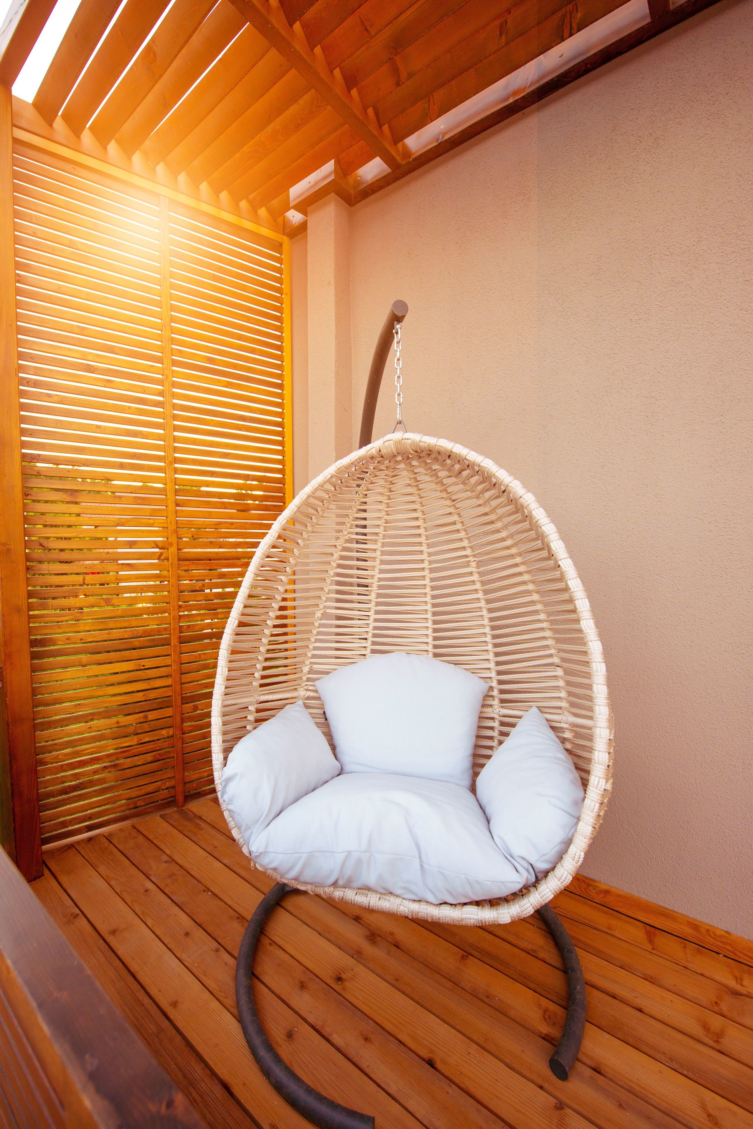 A wicker hanging chair with cushions on a wooden deck.