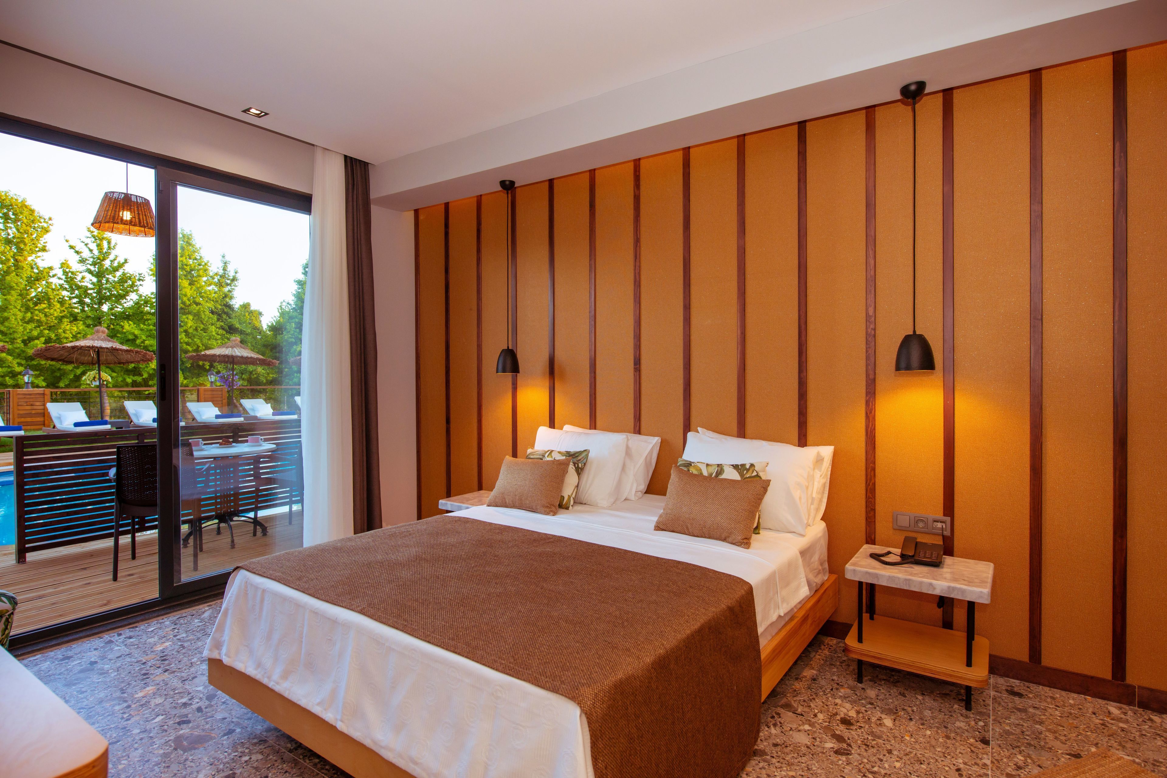 A modern hotel room with a large bed, a bedside table, and a view of an outdoor pool area.