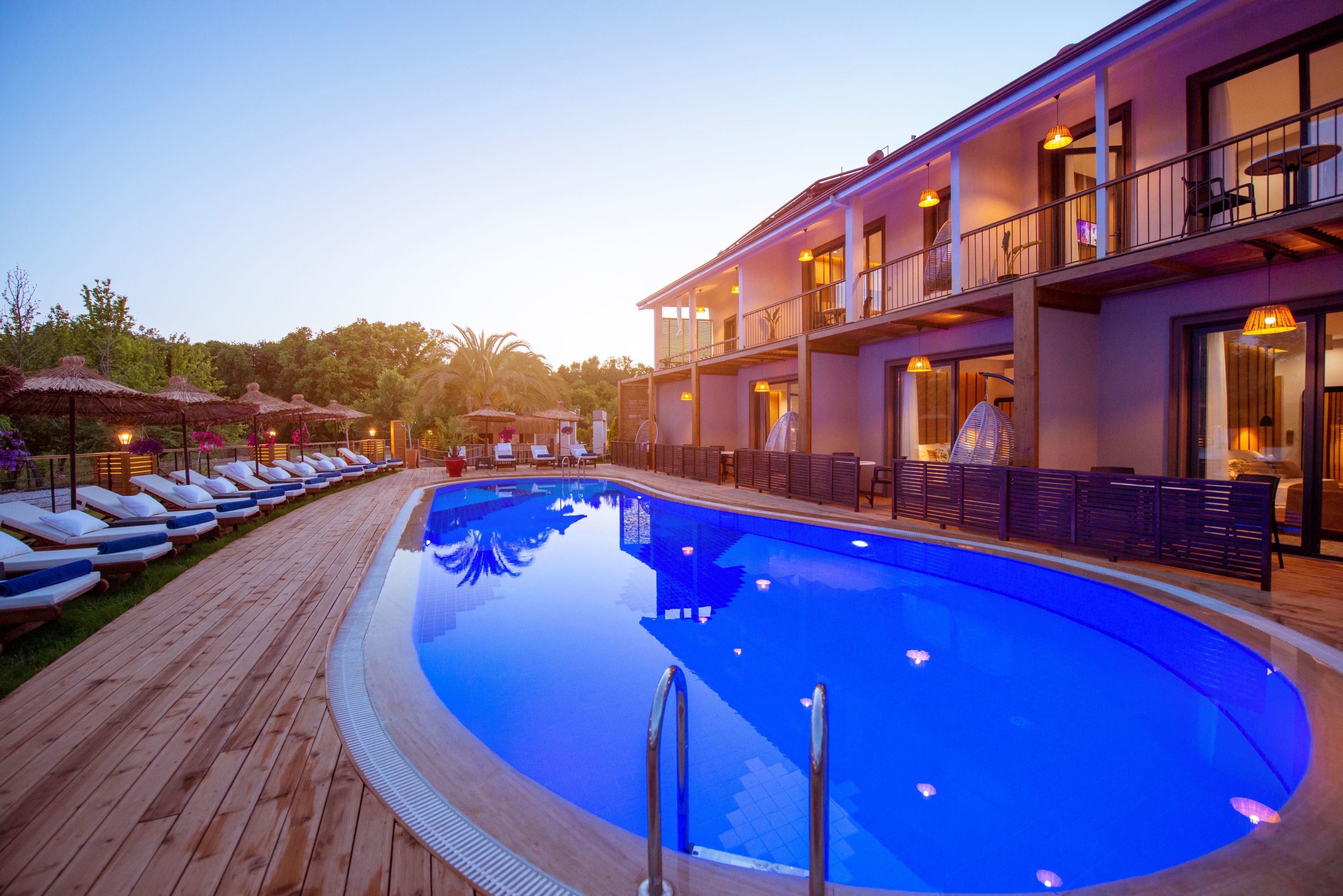 A swimming pool with lounge chairs and umbrellas, a building with balconies and outdoor seating, and a clear sky.