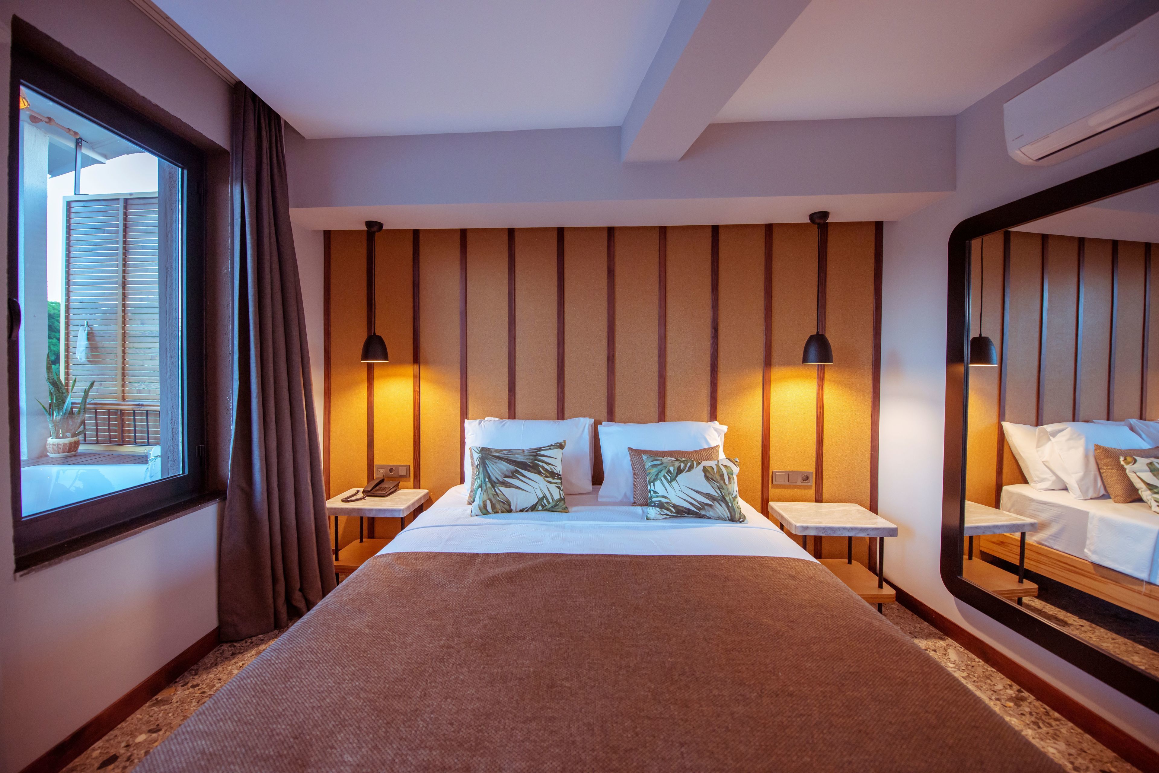 A hotel room with a large bed, two bedside tables, a nightstand, a mirror, and a window with curtains.