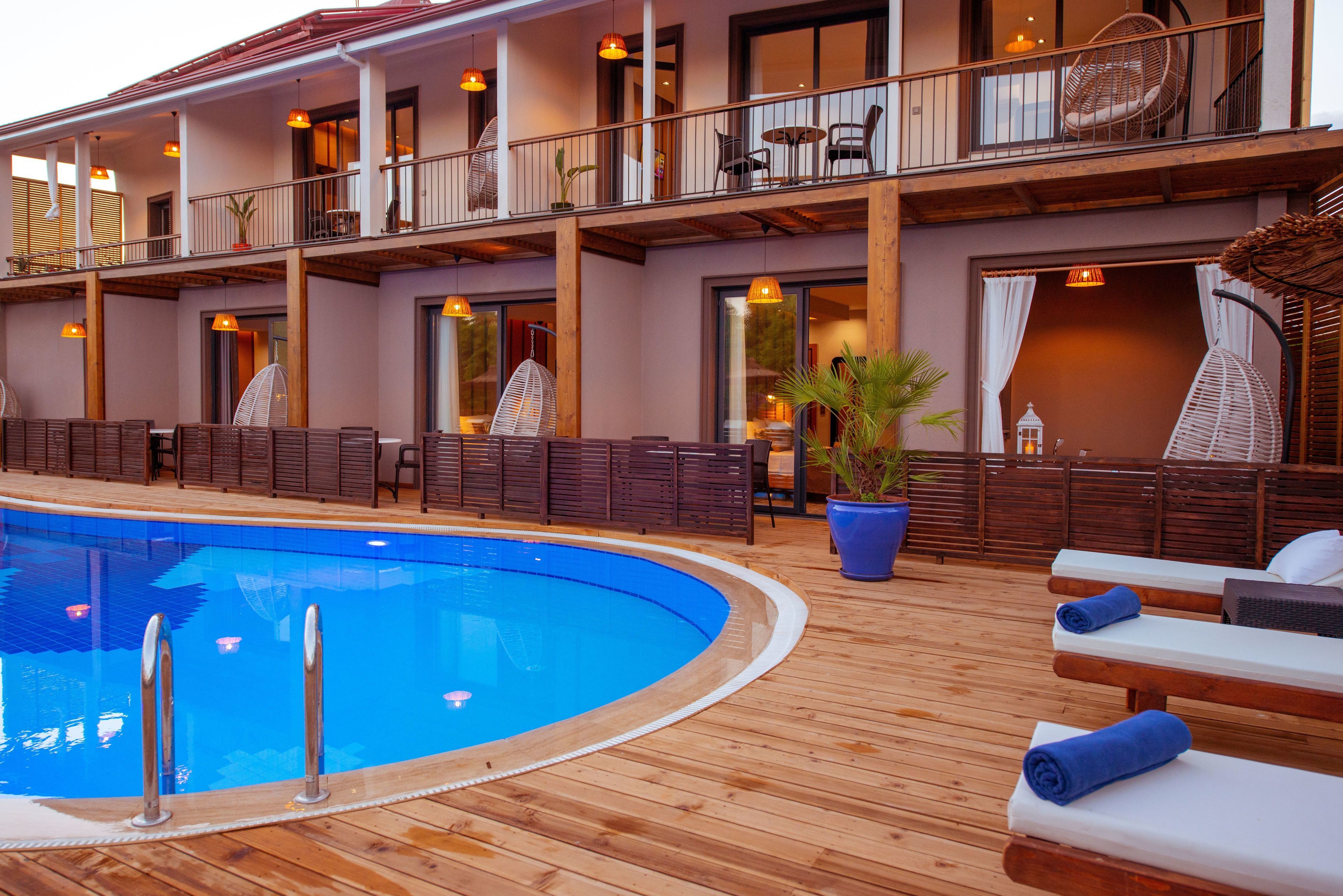 A poolside area with lounge chairs and a wooden deck, overlooking a building with balconies and large windows.