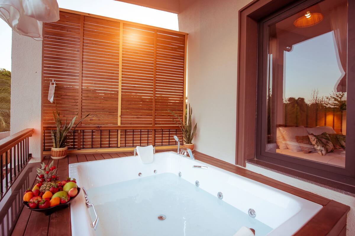 Un área de spa con un jacuzzi, terraza de madera, plantas en macetas y vistas al exterior.