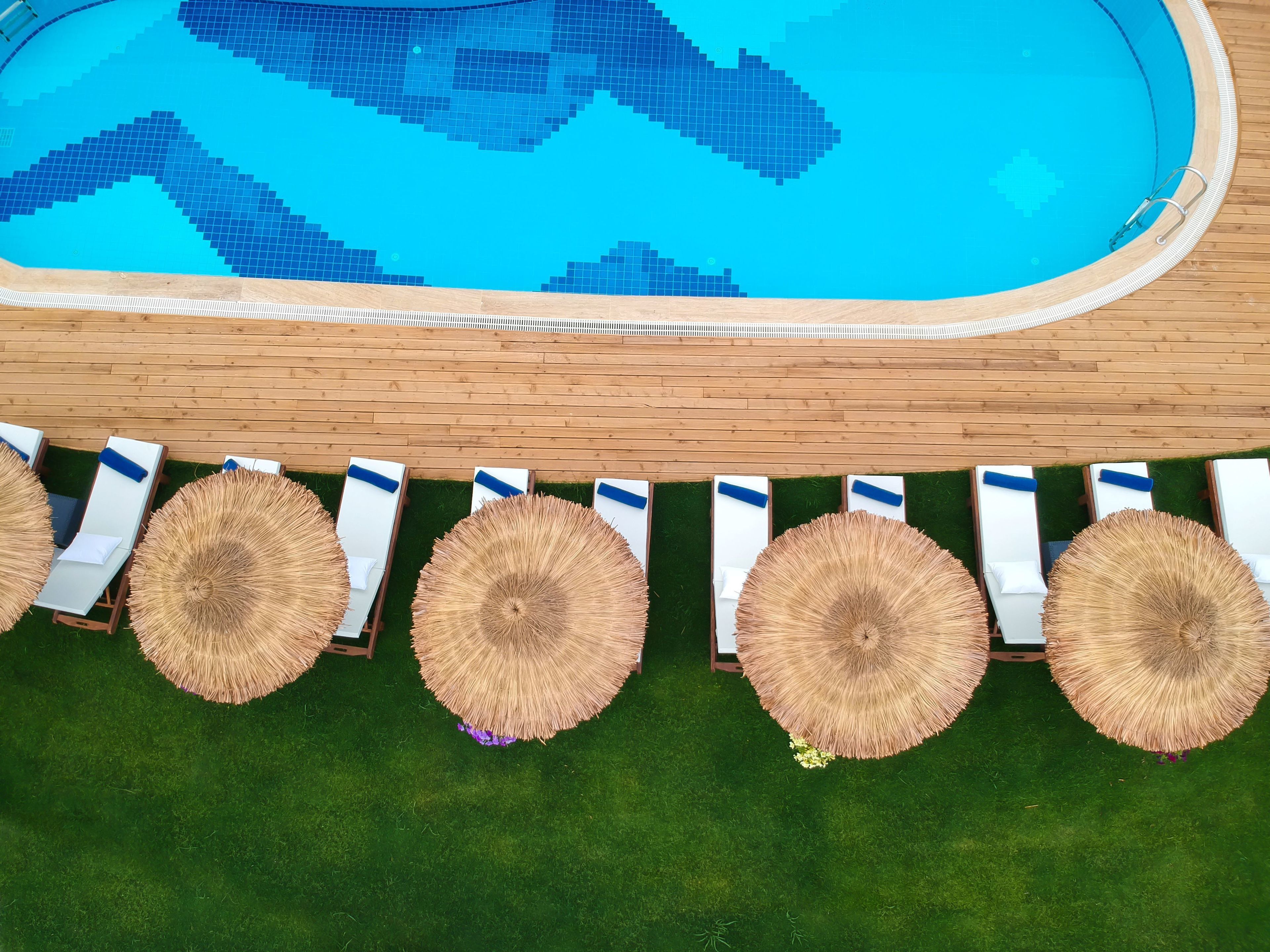 A poolside area with a tiled pool, lounge chairs, and thatched umbrellas.