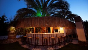 A thatched-roof bar with stools, surrounded by palm trees and a clear sky. - Arwen Hotel (Fethiye)