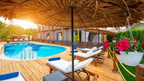 A wooden deck with a pool, lounge chairs, and a thatched umbrella. - Arwen Hotel (Fethiye)