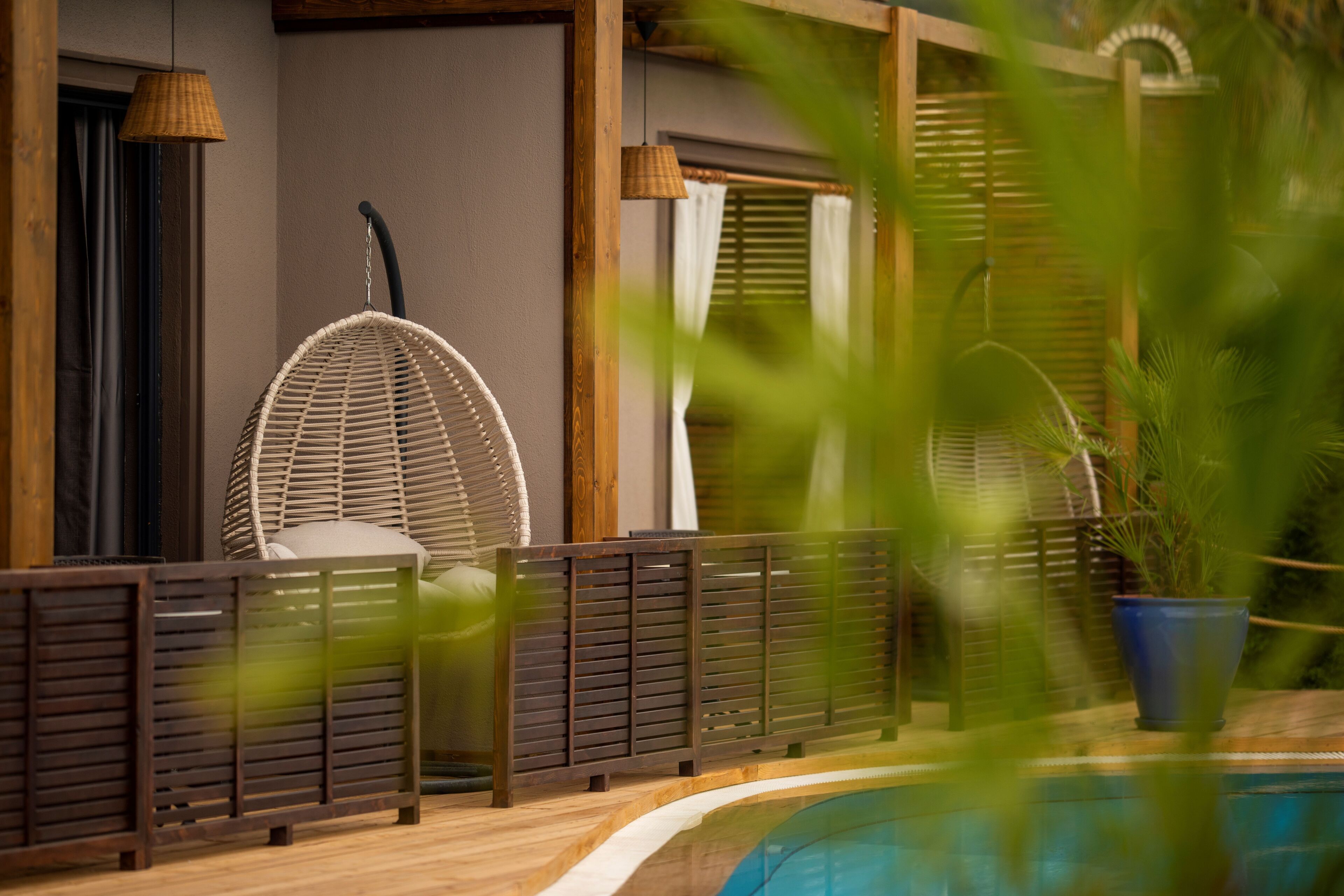A poolside area with a wicker chair, wooden deck, and a potted plant.