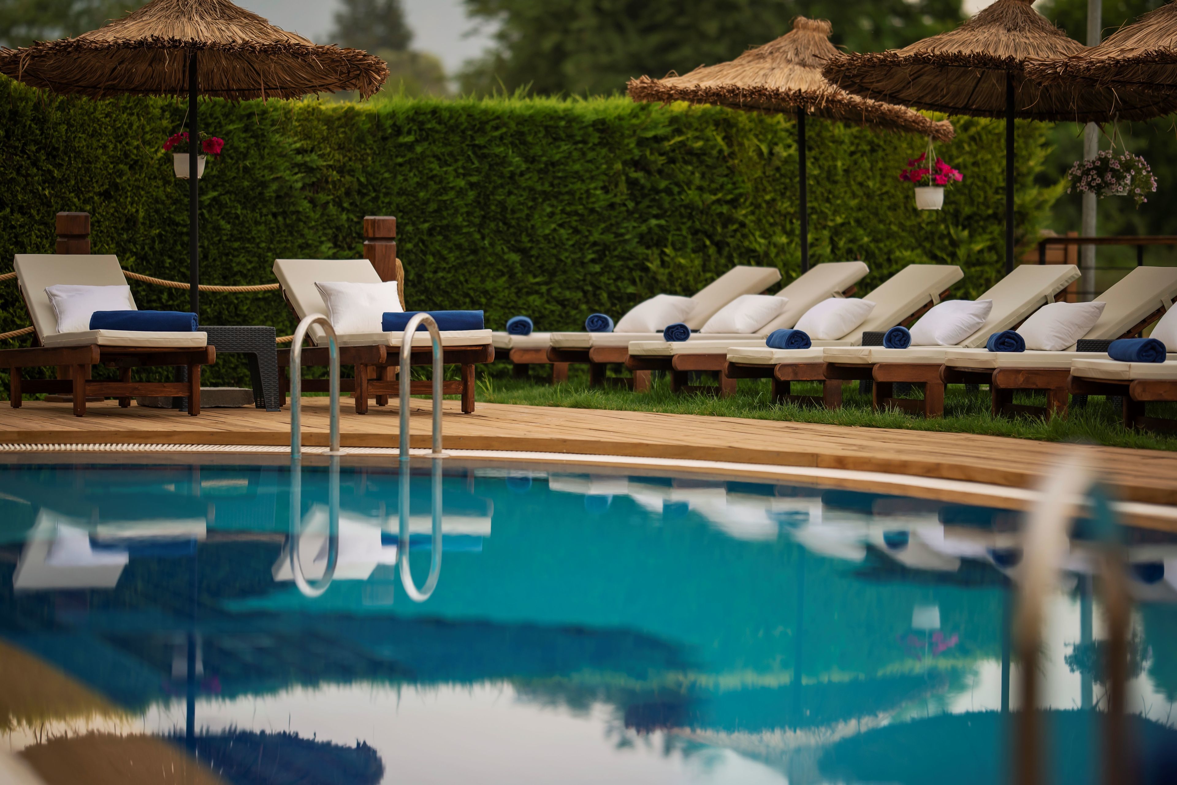 Un área junto a la piscina con sillones de descanso y sombrillas de paja.