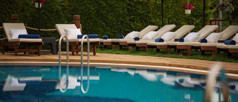 Un área junto a la piscina con sillones de descanso y sombrillas de paja.