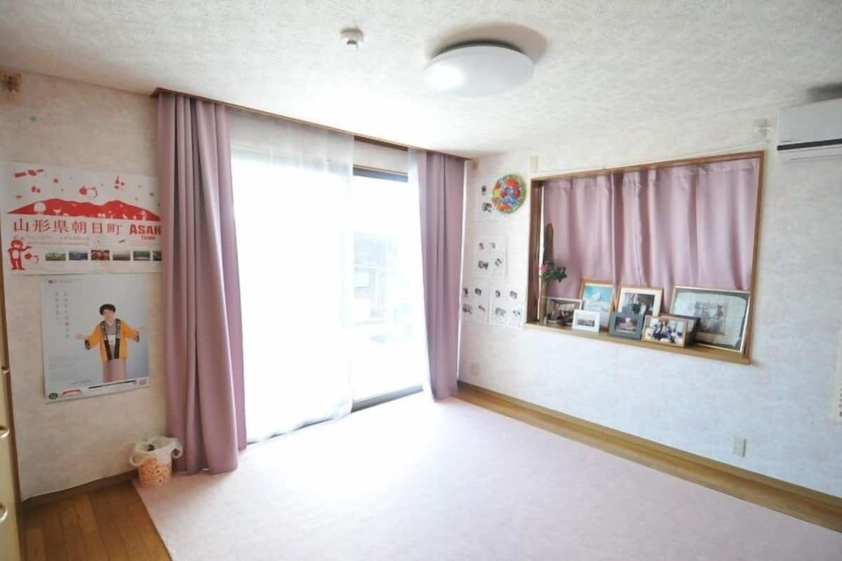 A room with a large sliding door, a window with curtains, a wall-mounted shelf with photos, and a ceiling light.