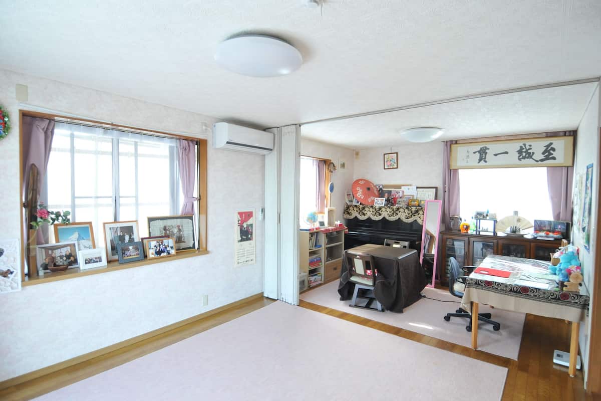 A room with a desk, chair, shelves with books, a piano, and a window with curtains.