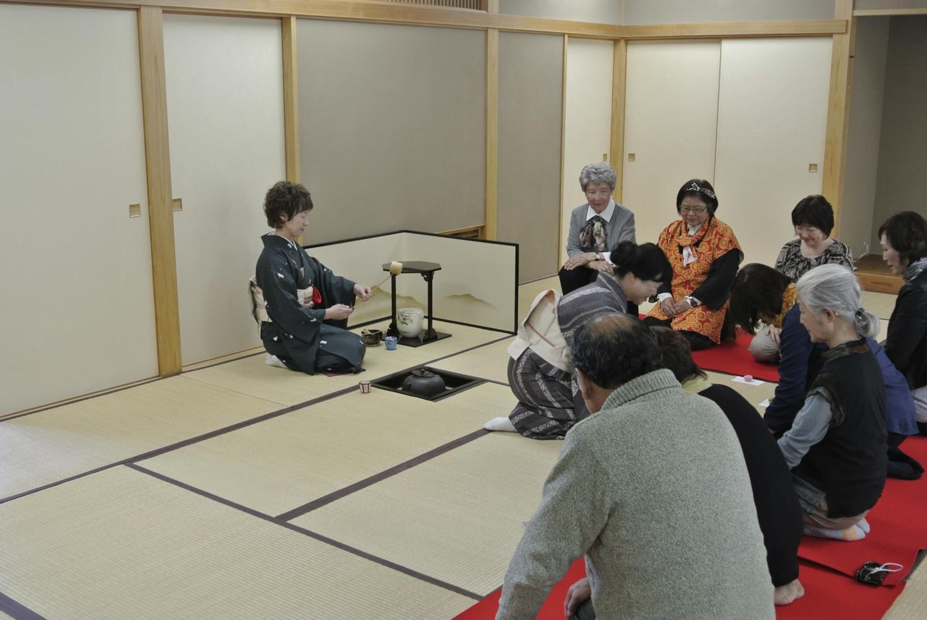 Una habitación con esteras de tatami y una disposición tradicional para la ceremonia del té japonesa, que incluye un calentador de agua y un juego de té sobre una mesa baja.